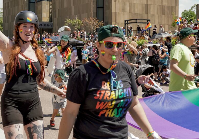 Pride parade participants one girl with long red heair and a black helmet in black t-shirt and shorts with tattoos on her legs and another woman wearing a black t-shirt with the words 