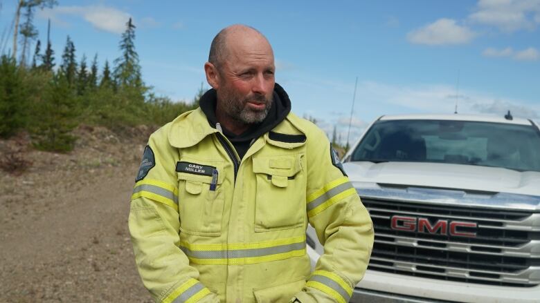 Man stands in front of a white truck wearing yellow coveralls. 