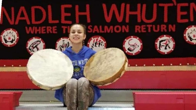 A woman sits in bleachers holding up two large, round drums.