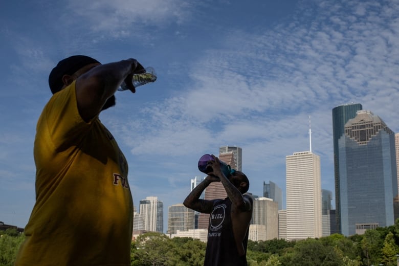 People drink from water bottles as tall buildings are seen behind them.