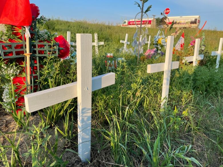 White crosses are seen in green grass as a semi-truck drives by in the background.