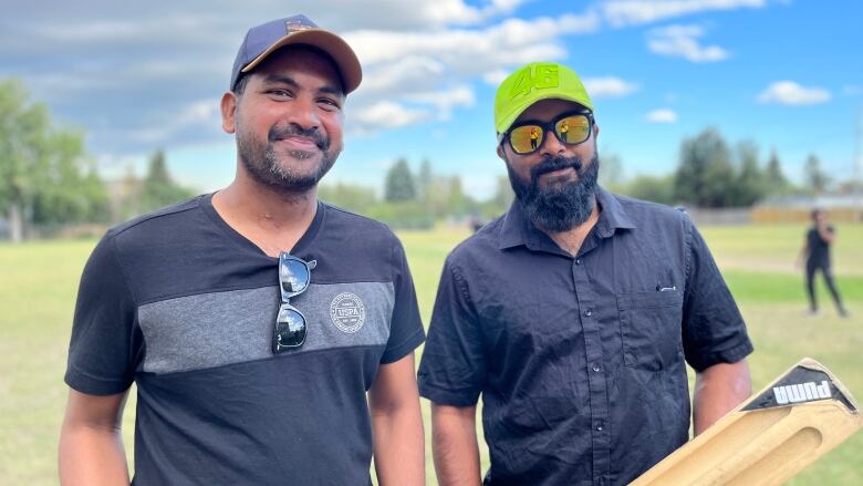 Two men in dark shirts smile for the camera.