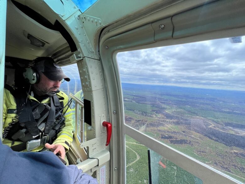 A man in yellow looks out a helicopter window