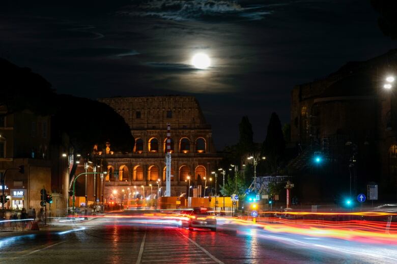 Full moon rising over the Colosseum and the Roman Forum in Rome, with traffic on the road in the foreground.