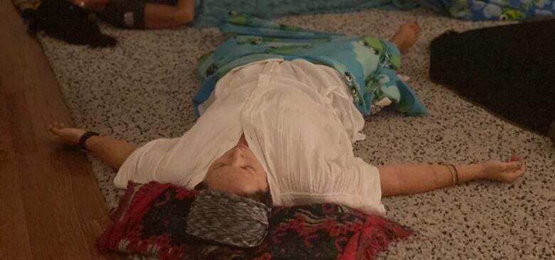 A woman lays on a carpet on her back with her arms spread wide and eyes closed.