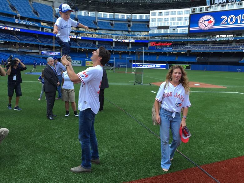 A father tosses his son in the air on a baseball diamond.