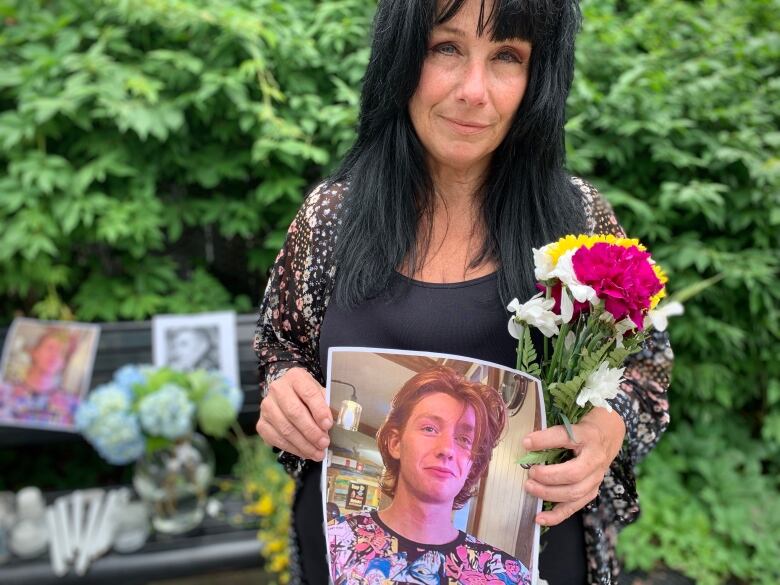 Woman holds flowers and picture of boy 