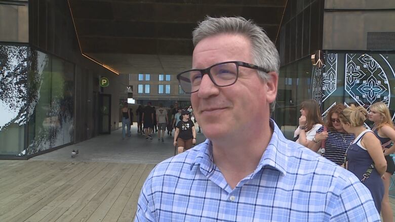 A man in a checked blue shirt speaks to the camera.