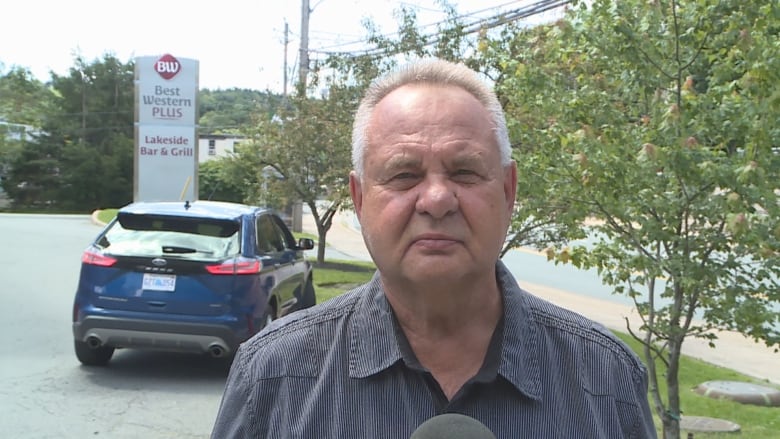 A man stands in front of a Best Western Plus sign and speaks to the camera.