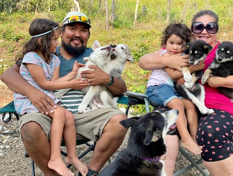 A family sits outside in lawn chairs holding a bunch of puppies.