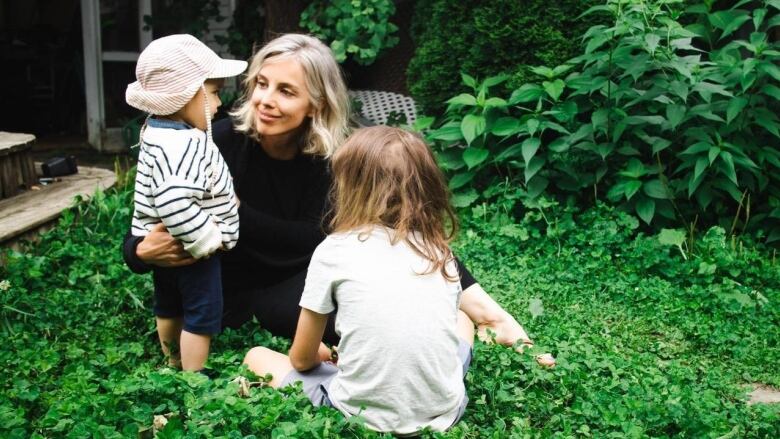 A woman has her arms around two children in a garden.