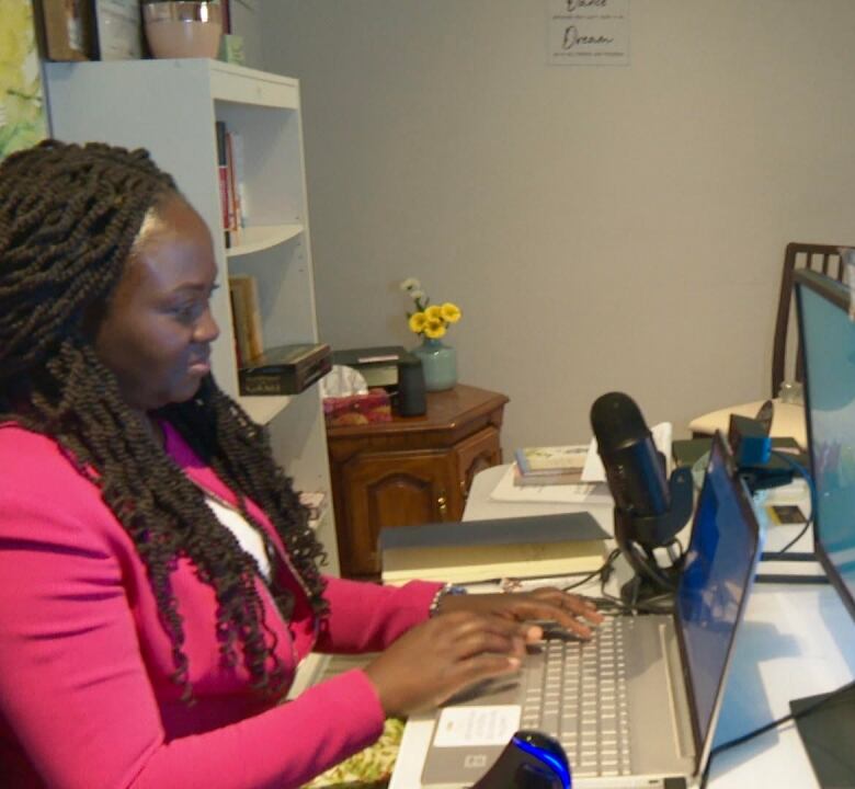 A woman sitting behind a table in a room and working on her lap top.