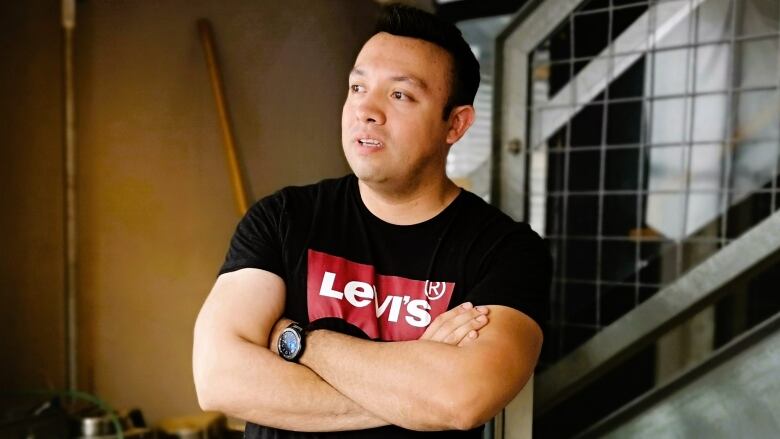 Chef Fernando Toro stands in his restaurant wearing a black shirt with his arms folded