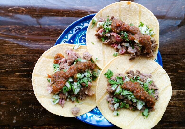 Carne asada tacos topped with an herb & onion mixture and red salsa