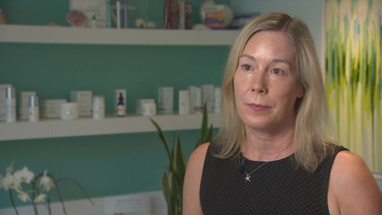 A woman stands behind shelves of items and looks off camera.