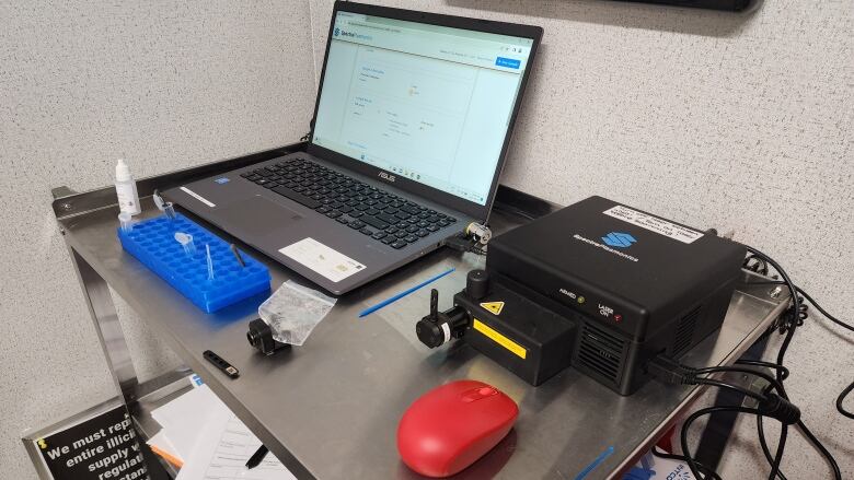 A laptop, mouse and black box that will collect the sample on a metal table. 