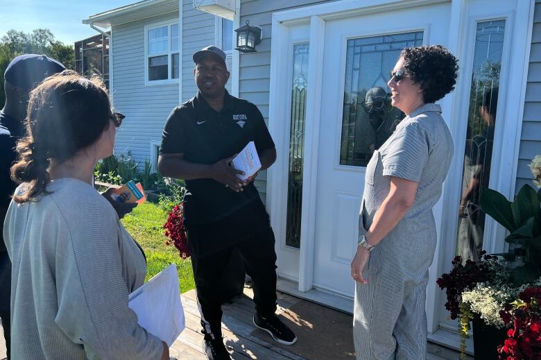 Four people stand by the front door of a home. One of them holds an election campaign  brochure.