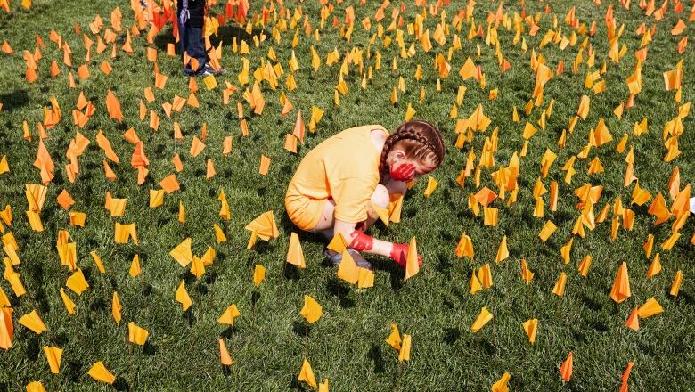 A young girl in an orange shirt is seen planting orange flags in the grass, among a sea of other orange flags.