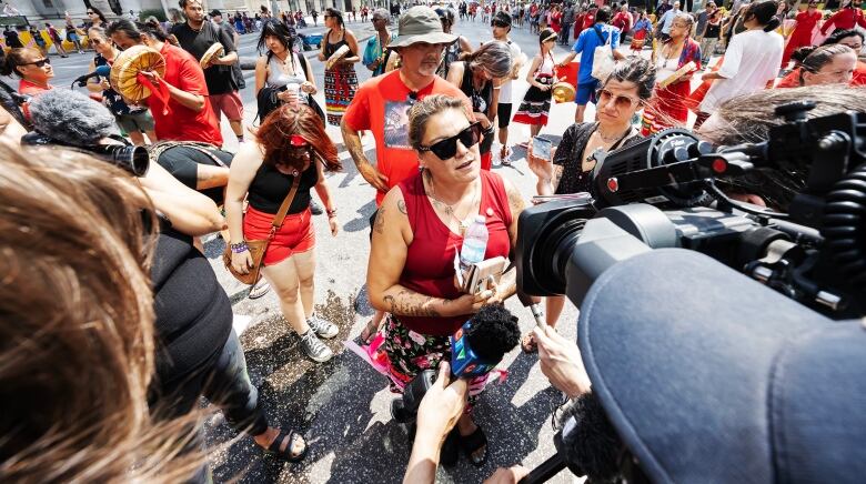 A woman is shown speaking to reporters as a large crowd gathers behind her.