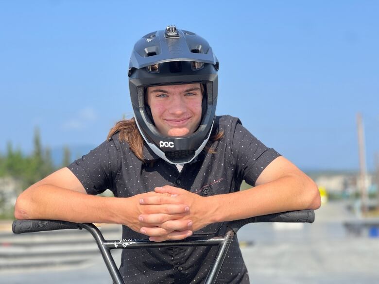 A teenaged boy in a helmet lean on the handlebars of a bike.