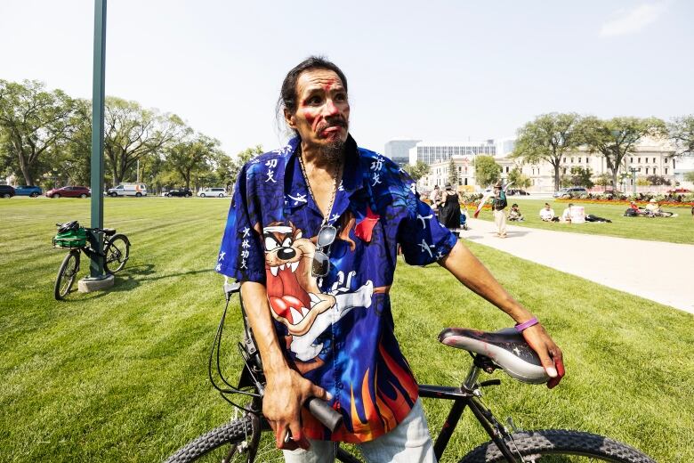 A man looks on, while holding onto the seat of his bicycle.