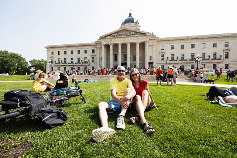 A married couple sits on the grass, while a rally behind them.