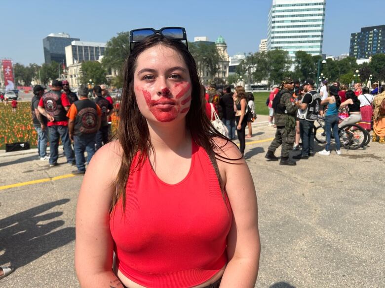 A woman with a red handprint painted on her face poses for a photo.