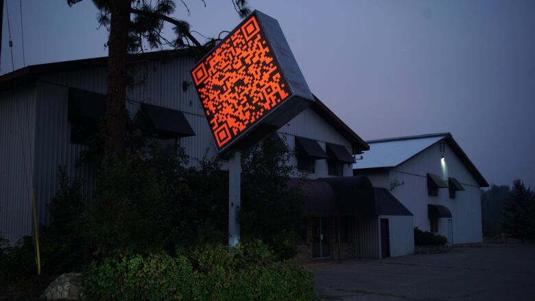 Exterior of a building, the Cardiff Miller Art Warehouse, at dusk. A large sign shaped like an orange QR code, is in front of the building.