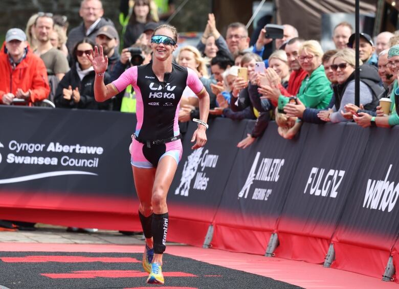 Woman in athletic gear runs down a path in front of an applauding audience behind a guardrail.