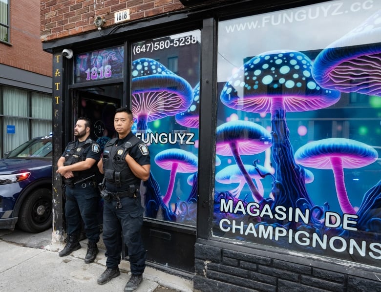 Two uniformed police officers stand in front of the door to a shop with purple signs.