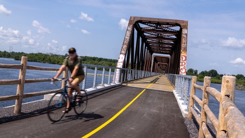 A smiling cyclist bikes over a new bridge.