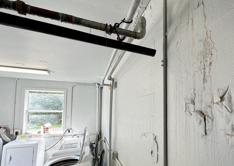 A white concrete laundry room is shown with a leaking water pipe in the ceiling.