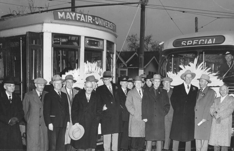 A black and white photo shows men in overcoats and hats standing in front of a streetcar with Mayfair-University on it