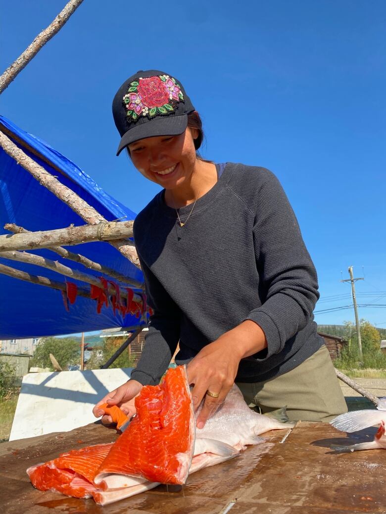 A smiling woman in a hat processes salmon.