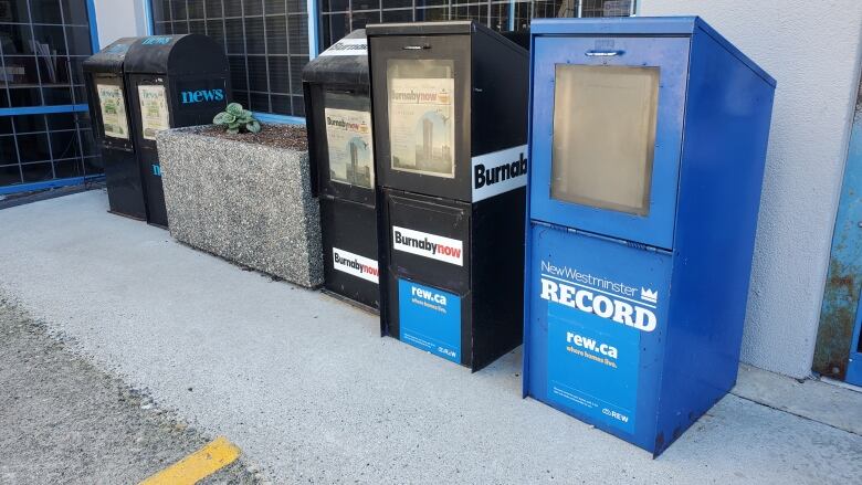 News boxes sit on a sidewalk.