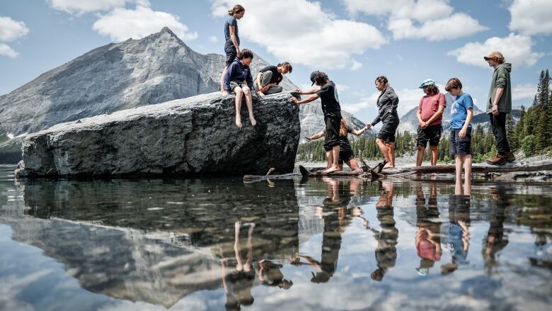 Participants cross over a log and rock bridge they constructed to reach a large bolder in Upper Kananaskis Lake.