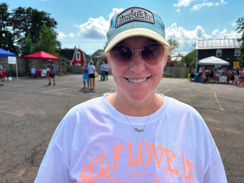 Colleen VanIderstine, a volunteer at the community fridge, smiles in a photo. She wears a white T-shirt, hat and sunglasses. 