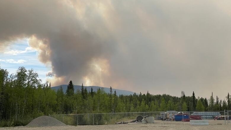 Smoke blots out the sky above a roadside dirt lot.