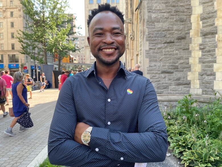 A man wearing a heart Pride pin smiles at the camera. 