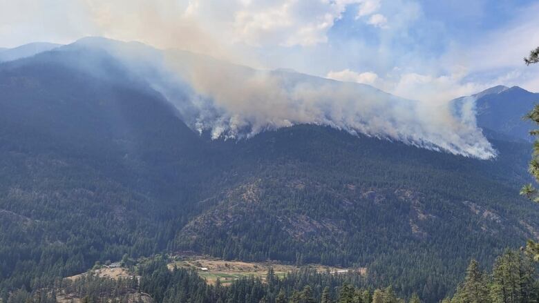 Smoke plumes are seen at the top of a forested mountain.