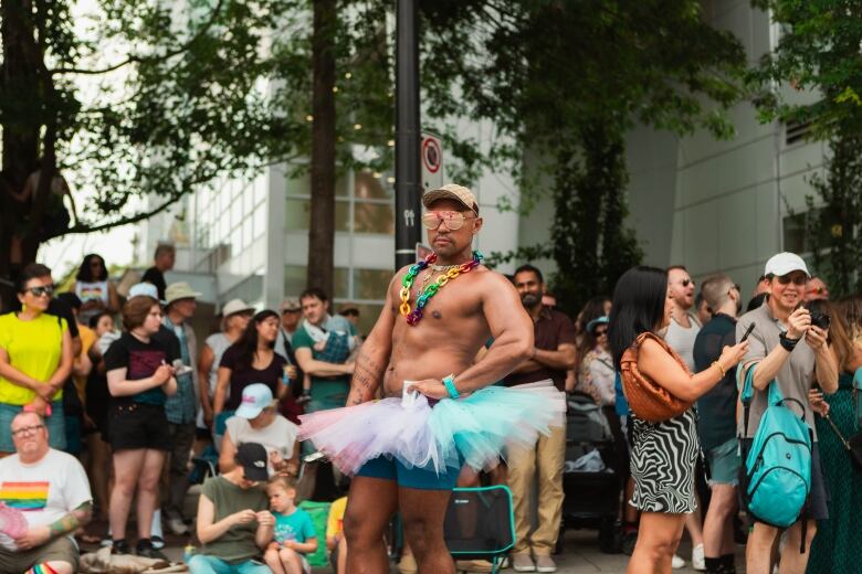 A man is pictured in a rainbow tutu and rainbow jewelery posing. 