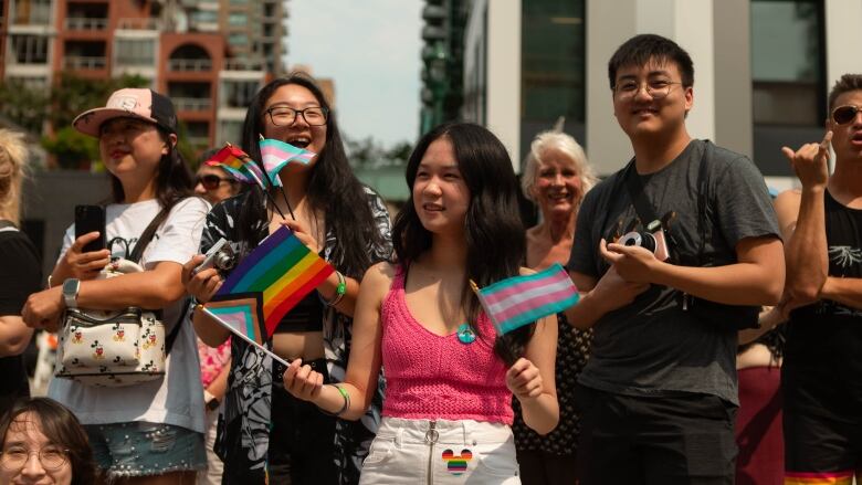 A person holds up a rainbow pride flag in one hand and a transgender pride flag in the other. 