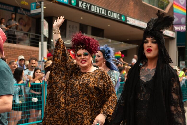 Two people dressed in drag are pictured walking along the parade route. 