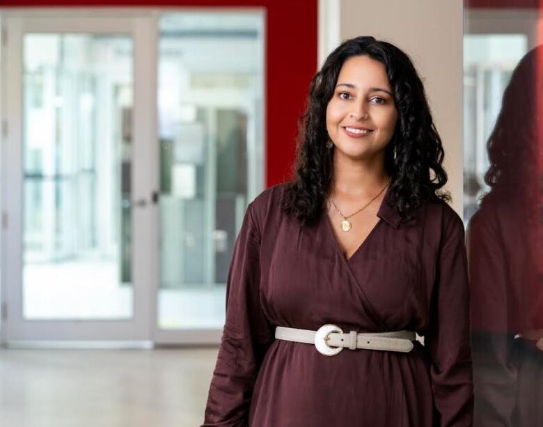 A woman in a purple dress and while belt stand in the student offices at the University of Calgary.