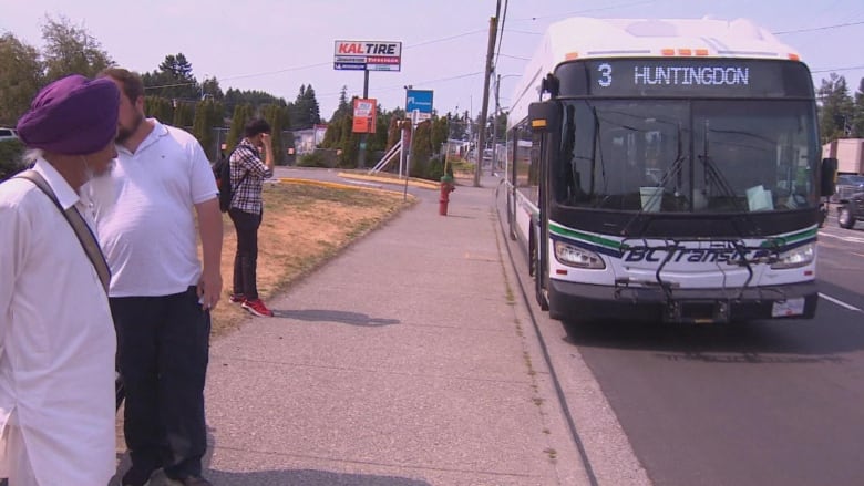 A bus pulls up to a stop with people waiting.