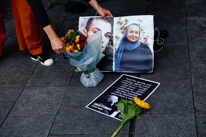 A person sets a bouquet of flowers down next to two photos of the same woman during different periods of her life.