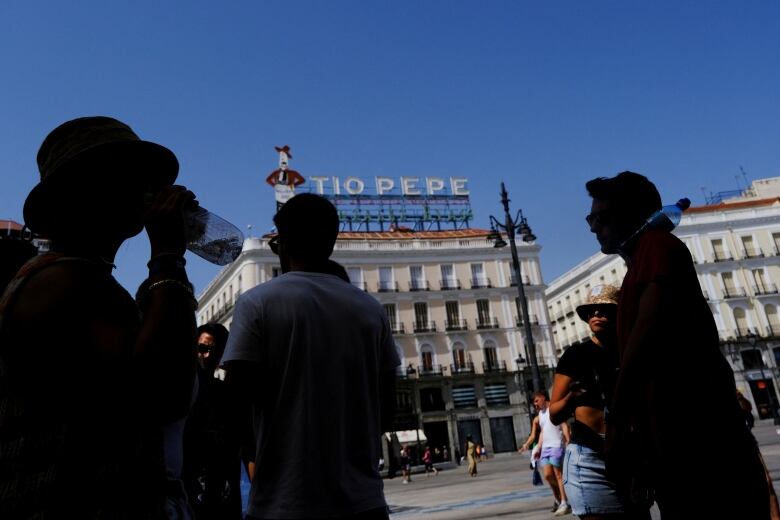 People are seen silhouetted in shade.