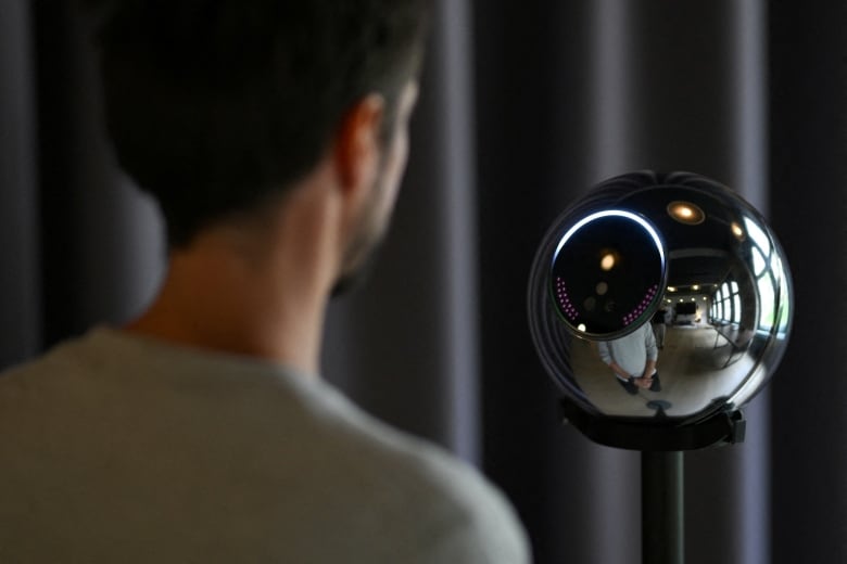 A man's back as he faces a metallic orb with a black window. 