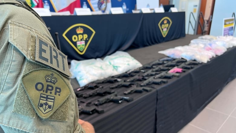 OPP officer stands in front of seized weapons and drugs.