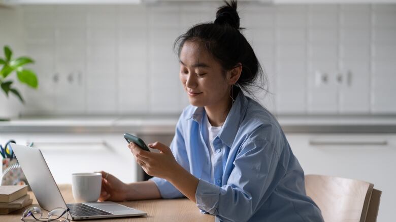 A smiling woman sitting at a desk holding a smartphone.